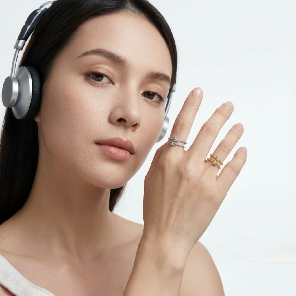 Close-up of a woman in silver headphones raising her hand to show two twisted rope open rings with baguette-cut zircon stones in silver and gold tones against a clean white background