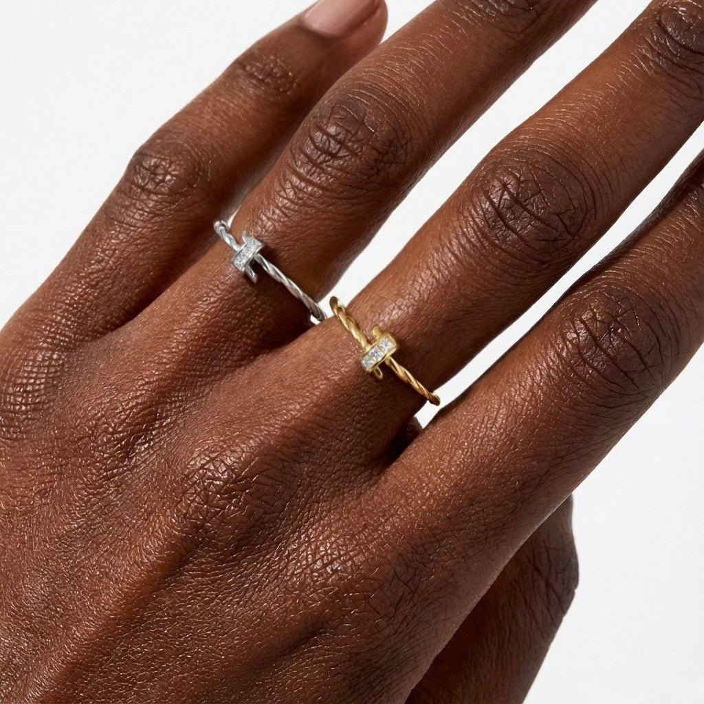 Close-up of a hand wearing two twisted rope adjustable rings in silver and gold tones, each set with zircon stones, stacked minimalist rings by OMŌN Jewelry.